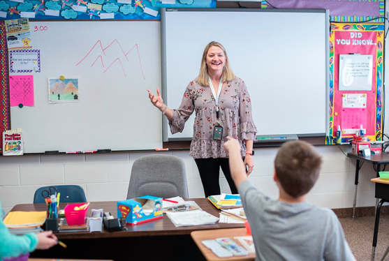 Teacher standing in front of white board, student with raised hand